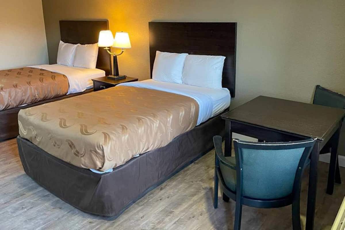A hotel room with two beds, a desk, and a chair.