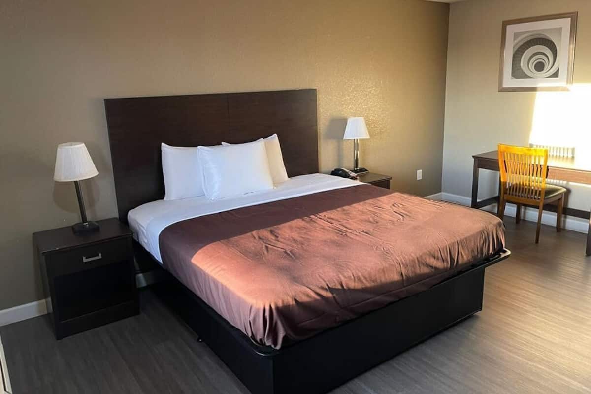 A hotel room with a large bed, two bedside tables, a chair, and a desk with a lamp.
