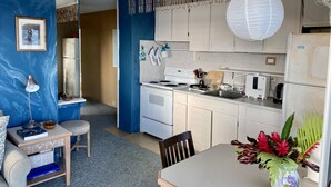 Une cuisine compacte avec des appareils électroménagers blancs, une table à manger agrémentée d’un vase de fleurs et un mur d’accent bleu.