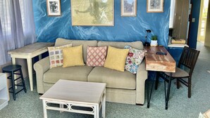 Un salon avec un mur bleu, un canapé, une table basse, une table à manger et des tableaux encadrés.