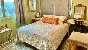Une chambre à coucher comprenant un lit, un bureau, une chaise, une fenêtre avec des rideaux et un tableau encadré accroché au mur.
