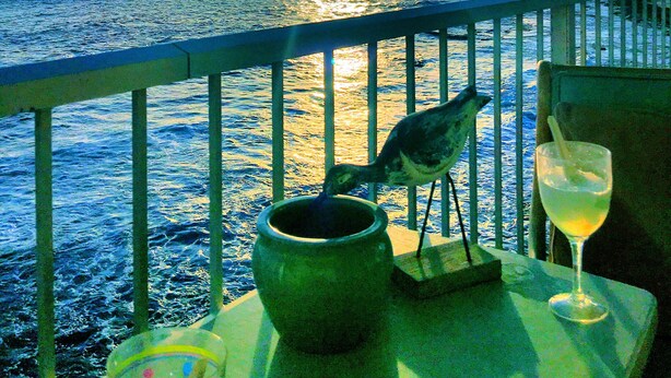 Une vue sur le coucher de soleil depuis un balcon, avec une mangeoire à oiseaux, un verre et un vase décoratif.