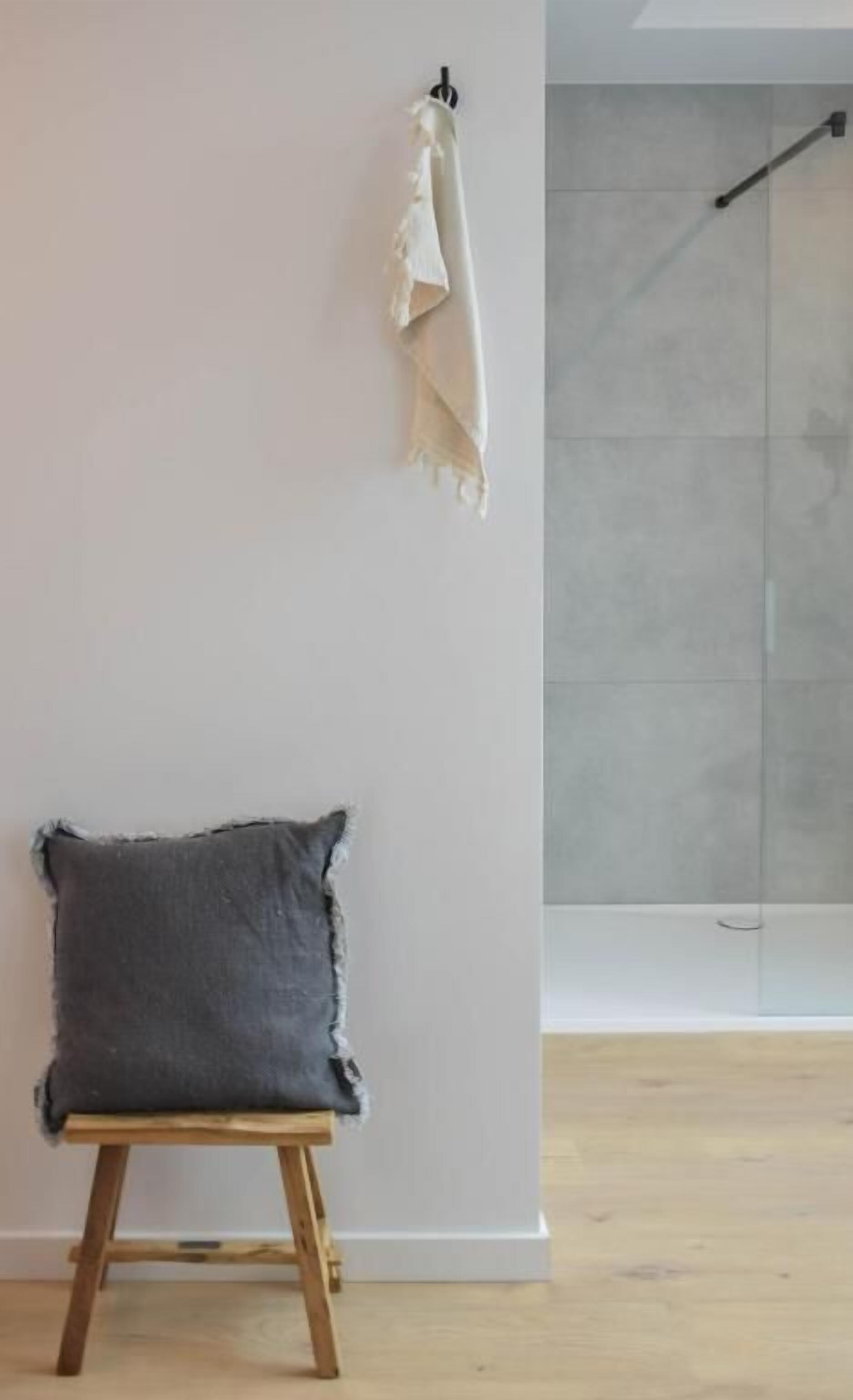 A room with a wooden stool, a white wall, and a shower area.