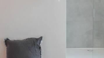 A room with a wooden stool, a white wall, and a shower area.