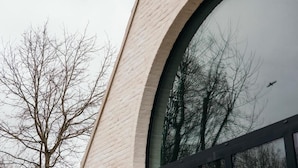 A building with a large arched window reflecting trees and a bird. - Factory Hotel (Beveren)