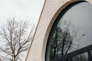 Um edifício com uma grande janela em arco refletindo árvores e um pássaro.