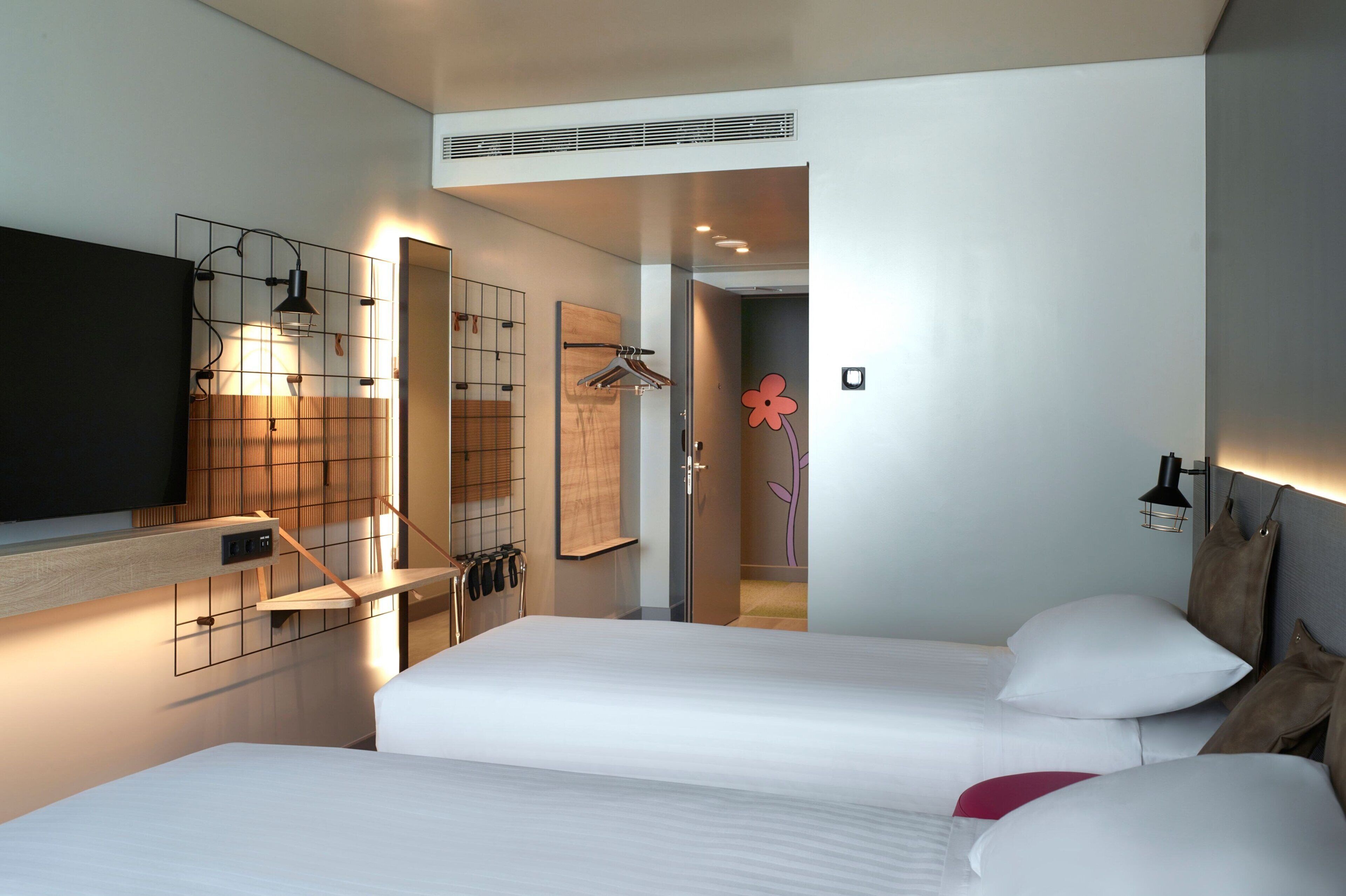 Une chambre d’hôtel moderne équipée de deux lits, d’une télévision, d’un miroir et d’un espace douche.