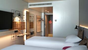 Une chambre d’hôtel moderne équipée de deux lits, d’une télévision, d’un miroir et d’un espace douche.