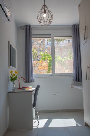 A small, bright room with a window, a desk, a chair, and a pendant light.