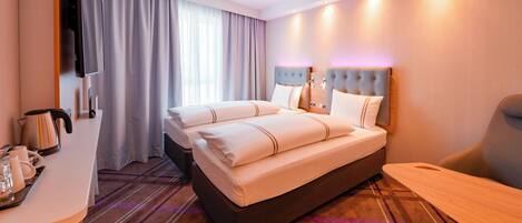 Habitación de hotel con cama, escritorio, silla, televisión y ventana con cortinas.