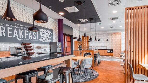 Ein moderner Frühstücksbereich mit einer Bar, Hockern und einer Sitzecke mit Tischen und Stühlen.