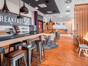 A modern breakfast area with a bar, stools, and a seating area with tables and chairs. - Premier Inn Mannheim City Centre (Mannheim)