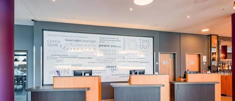 A hotel reception area with three counters, a large wall with text and phrases related to sleep and relaxation, and a bar area in the background.