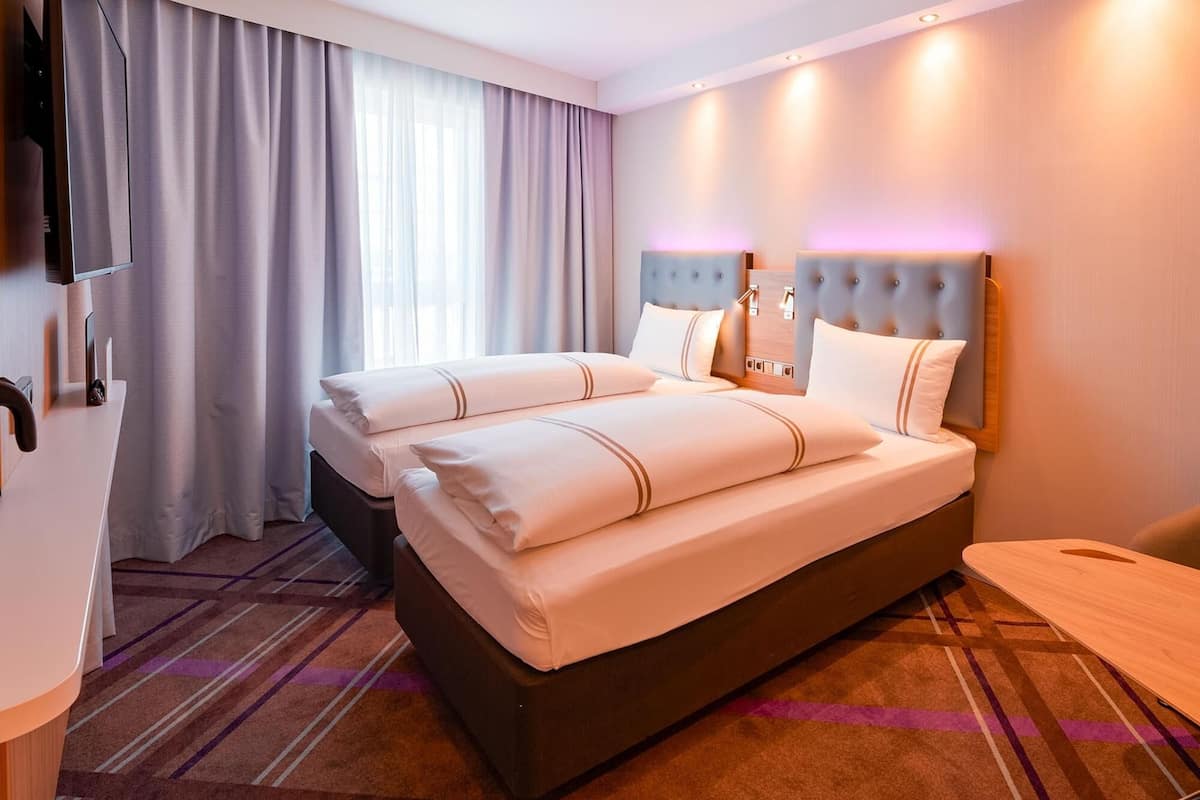 Ein Hotelzimmer mit einem großen Bett, einem Flachbildfernseher, einem Schreibtisch und einem Fenster mit Vorhängen.
