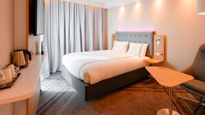 Ein Hotelzimmer mit Bett, Schreibtisch, Stuhl, Fernseher und einem Fenster mit Vorhängen.