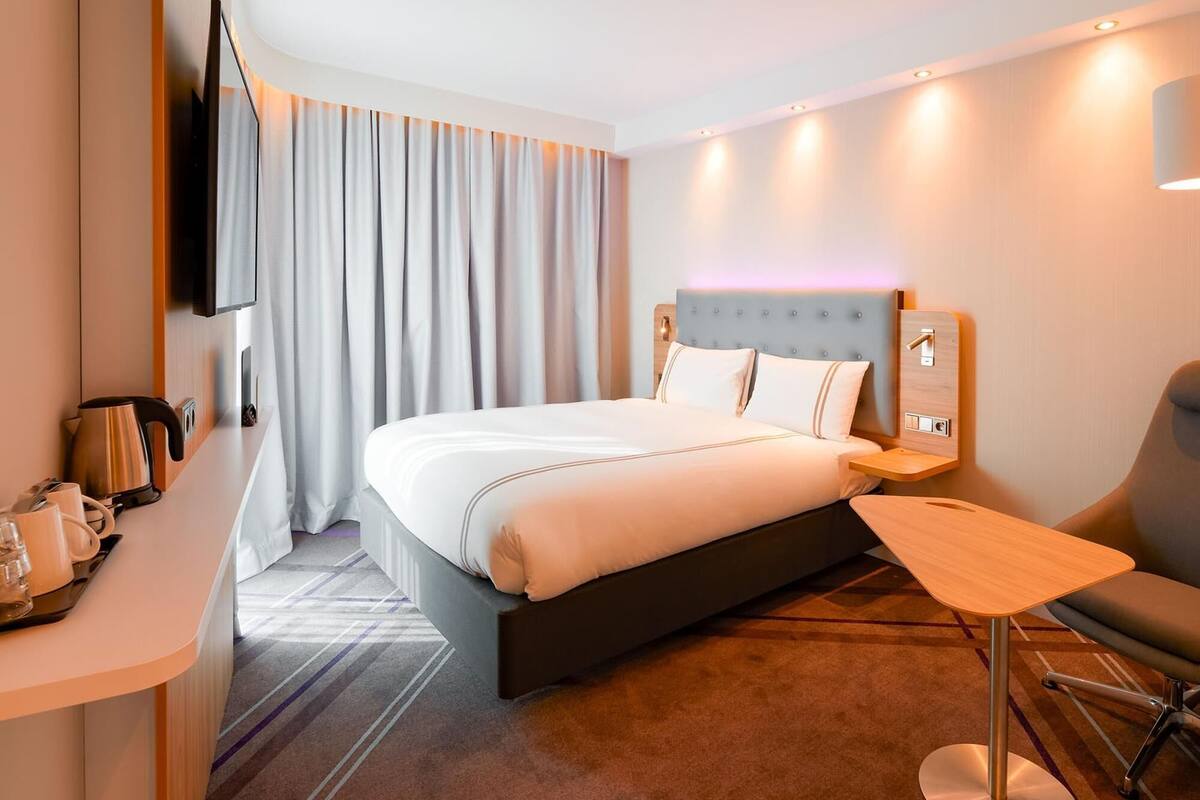Ein Hotelzimmer mit Bett, Schreibtisch, Stuhl, Fernseher und einem Fenster mit Vorhängen.