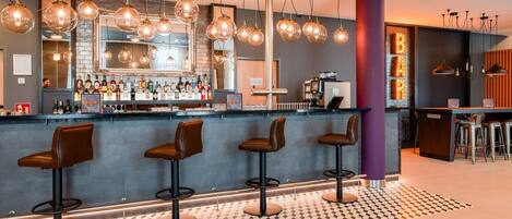 A bar area with a counter, stools, and hanging pendant lights.