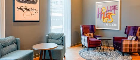 Una sala de estar moderna con un sofá gris, una mesa redonda y dos sillones. Hay dos obras de arte enmarcadas en las paredes.