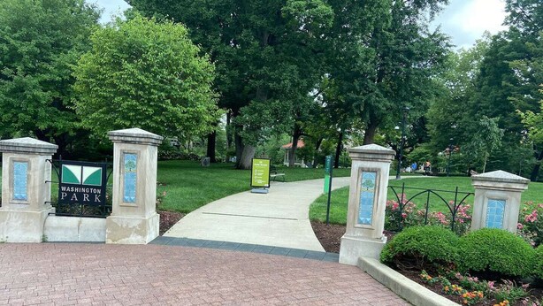 A paved entrance to Washington Park with a sign and two stone pillars.