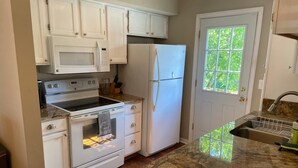 A kitchen with white cabinets, a microwave, a stove, a refrigerator, and a granite countertop.