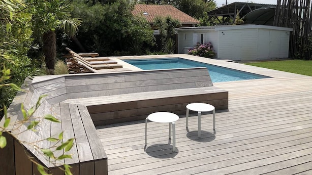 A wooden deck with a pool, two white tables, and a small garden area. - Magnificent villa with swimming pool in the center of Cap Ferret (CAP FERRET)