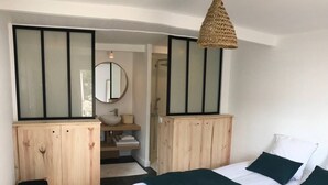 A bedroom with a bed, a wooden wardrobe, a small stool, a mirror, and a hanging light fixture. - Magnificent villa with swimming pool in the center of Cap Ferret (CAP FERRET)