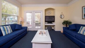 Ein Wohnzimmer mit zwei blauen Sofas, einem weißen Couchtisch, einem Fernseher und einer Tür mit Blick.