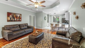 Un salon spacieux avec un canapé en cuir marron, un tapis à motifs et un ventilateur de plafond.