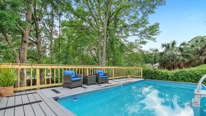 Une terrasse en bois avec une piscine, entourée d’arbres et de verdure.