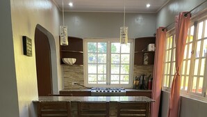 Una cocina con isla central, sillas de madera, estufa y ventana con cortinas.