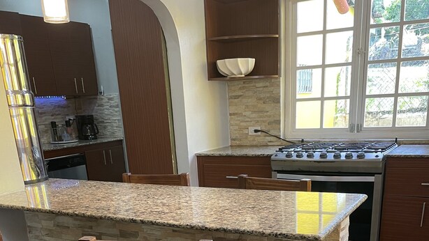Una cocina con encimera de granito, sillas de madera, estufa y salpicadero de piedra.