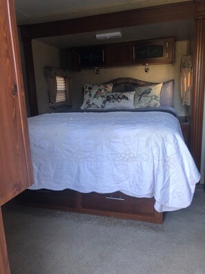 A bedroom with a bed, a nightstand, a lamp, and a window with curtains. - Finegold Escape (North Fork)