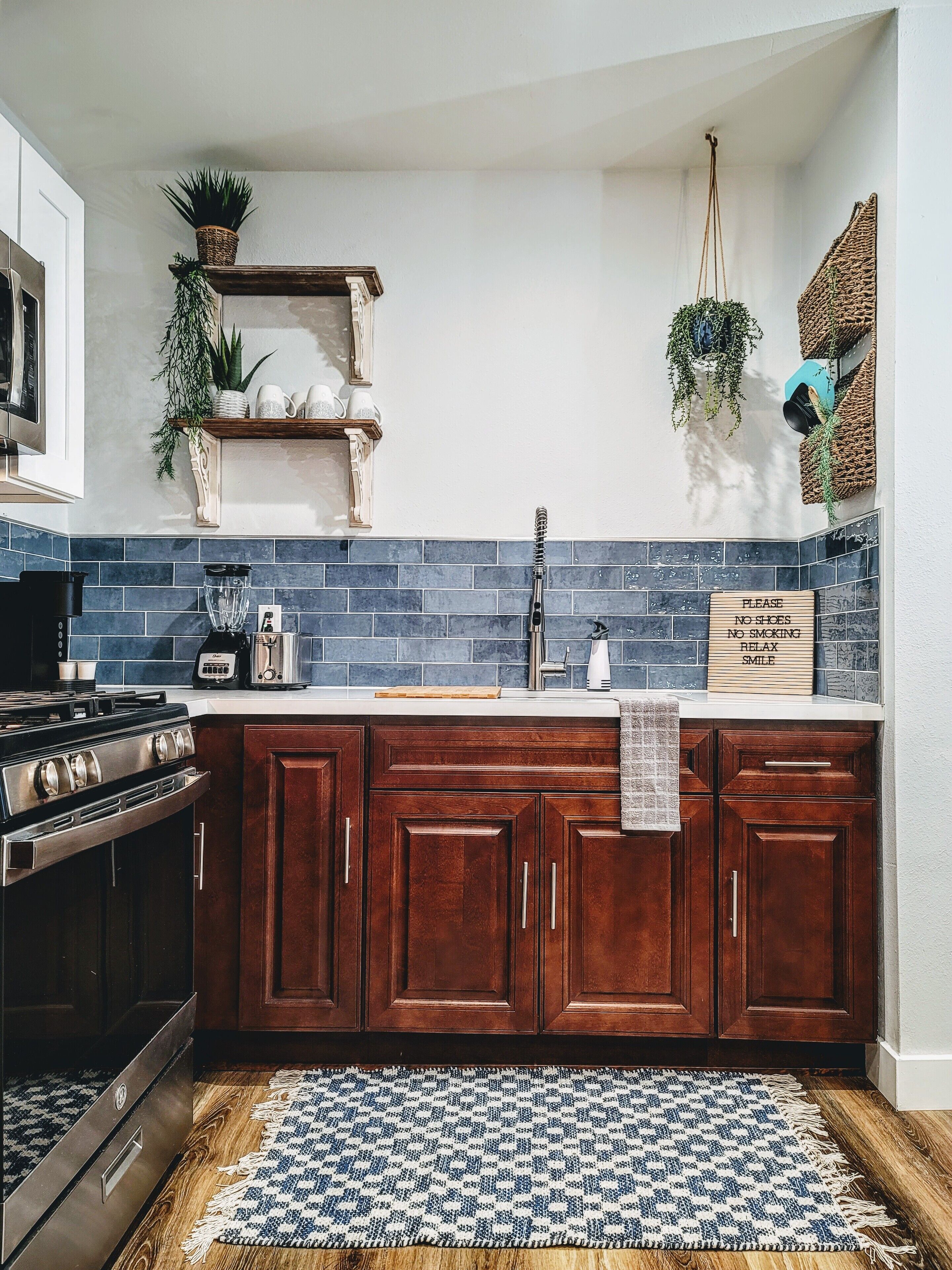 Een keuken met houten kastjes, een fornuis, een spoelbak en een blauwe betegelde achterwand.
