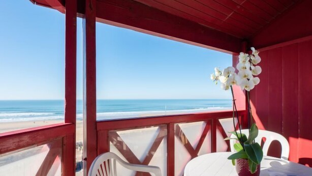 A beachside balcony with a white table and chairs, a potted orchid, and a view of the ocean. - Primavéra by Interhome (Lacanau)