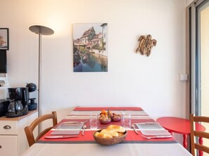 A dining area with a table set for two, a coffee maker, a basket of bread, and a bowl of nuts.