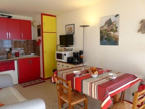 A compact kitchen with red cabinets, a yellow door, and a dining area with striped tablecloths and wooden chairs.