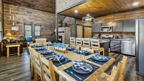 Un interior rústico de madera con un comedor preparado para seis personas, una cocina con electrodomésticos modernos y una chimenea.