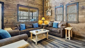 Una sala de estar acogedora con paredes de madera, dos sofás de cuero marrón con cojines azules, una mesa de centro de madera y un taburete pequeño de madera.