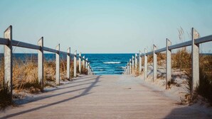 Un camí de fusta que condueix a la platja, amb una barana metàl·lica a cada banda.