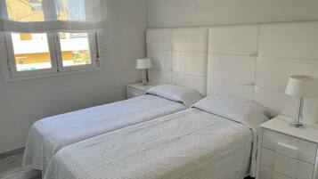 Una habitación con dos camas, una ventana y una mesita de noche con lámpara.