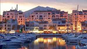 Un port esportiu amb nombroses embarcacions amarrades, envoltat d'edificis d'altes plantes amb balcons i una muntanya al fons.