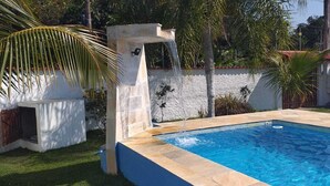 Una piscina con bordatura in pietra, una palma e un muro bianco sullo sfondo.