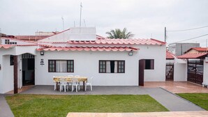 Una casa bianca con tetto in tegole rosse, un portico coperto con tavolo e sedie e un piccolo prato.
