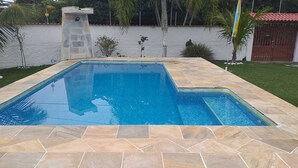 Una piscina rettangolare con bordo in pietra, circondata da un muro bianco e palme.