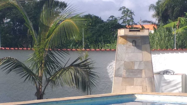 Una piscina con una struttura in pietra e un cane seduto sul bordo.
