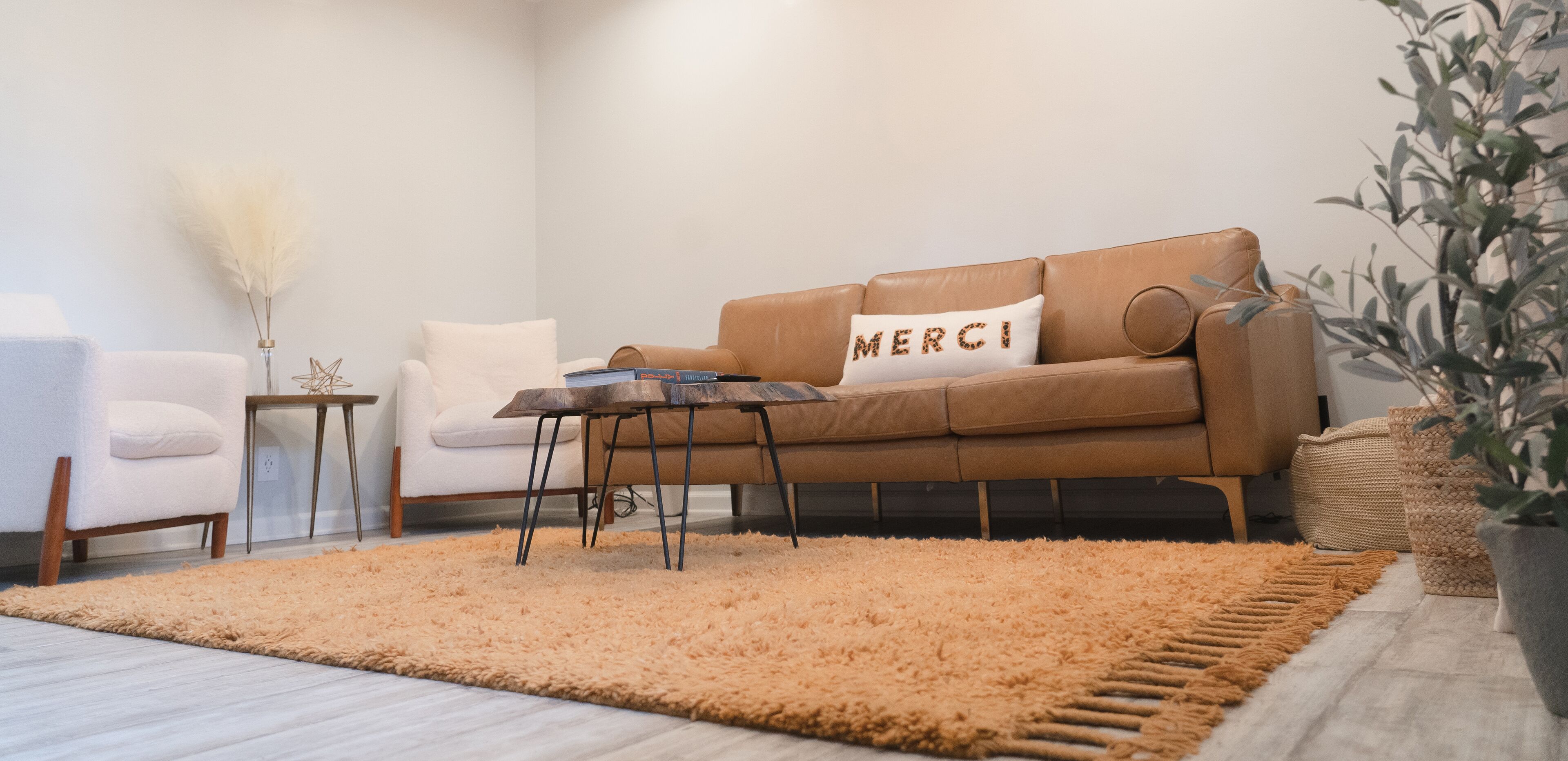 A modern living room with a brown leather sofa, a white armchair, a small wooden side table, and a fluffy orange rug.