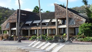 A resort with a modern architectural style, featuring a large building with multiple levels, a covered outdoor area with lounge chairs, and a landscaped garden with tropical plants.