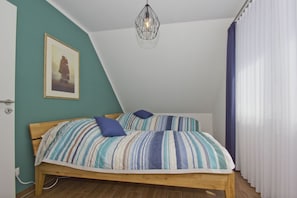 Une chambre avec un lit en bois, une literie à rayures, un luminaire suspendu, un tableau encadré au mur et une fenêtre avec des rideaux.