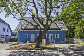 Un immeuble résidentiel à la façade bleue, doté d’un toit en tuiles et d’un arbre dans le jardin.