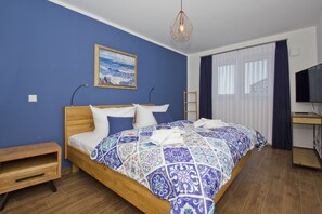A bedroom with a wooden bed, a blue wall, a painting of a sailboat, a desk with a TV, and a window with curtains. - Vacation home Luna - Holiday home Luna semi-detached house (Breege)